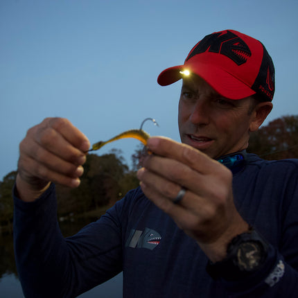 man wearing a pink LED lighted headlamp hat looking at fishing tackle