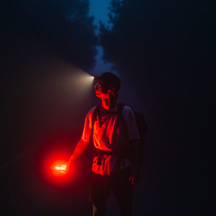 man walking in the woods at night holding a red flashlight and wearing an LED lighted hat