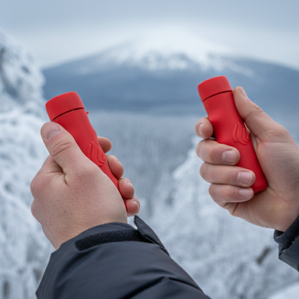 Two hands holding red POWERPAW 801 hand warmers in front of a snowy mountain