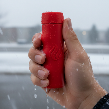 Wet hand holding a red POWERPAW 801 waterproof hand warmer in falling snow