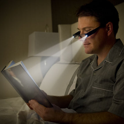 Person using lighted reading glasses to read a book while in bed