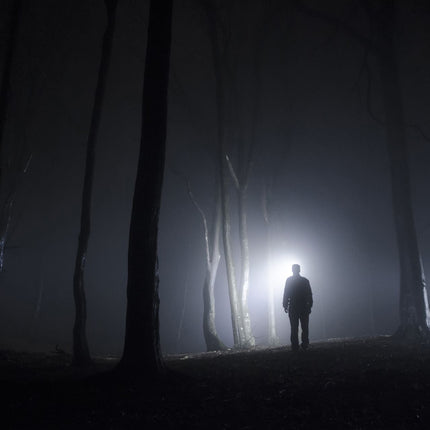 Person walking though a forest at night with an LED lighted cap