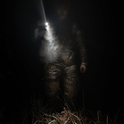 hunter walking through the woods at night holding a rechargeable LED flashlight