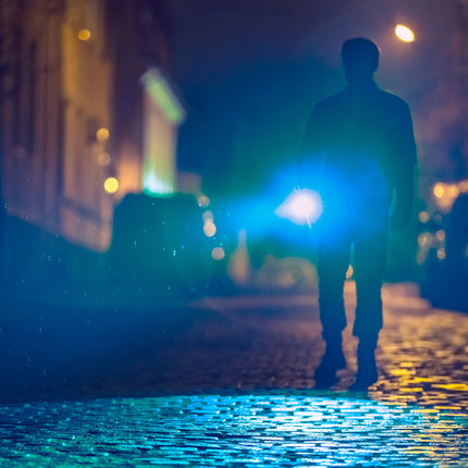 man walking at night on the street holding a rechargeable LED flashlight