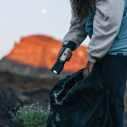 female hiker in the mountains looking in a hiking bag with a rechargeable LED lantern flashlight