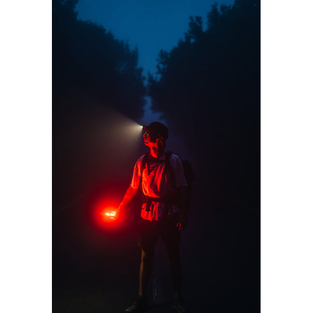 man walking in the woods at night with an LED lighted hat and red lantern flashlight