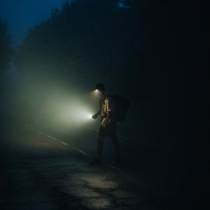 man walking at night in the road with an LED lighted hat and lantern flashlight
