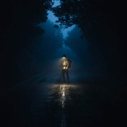 man walking on a road between trees at night with an LED lighted hat